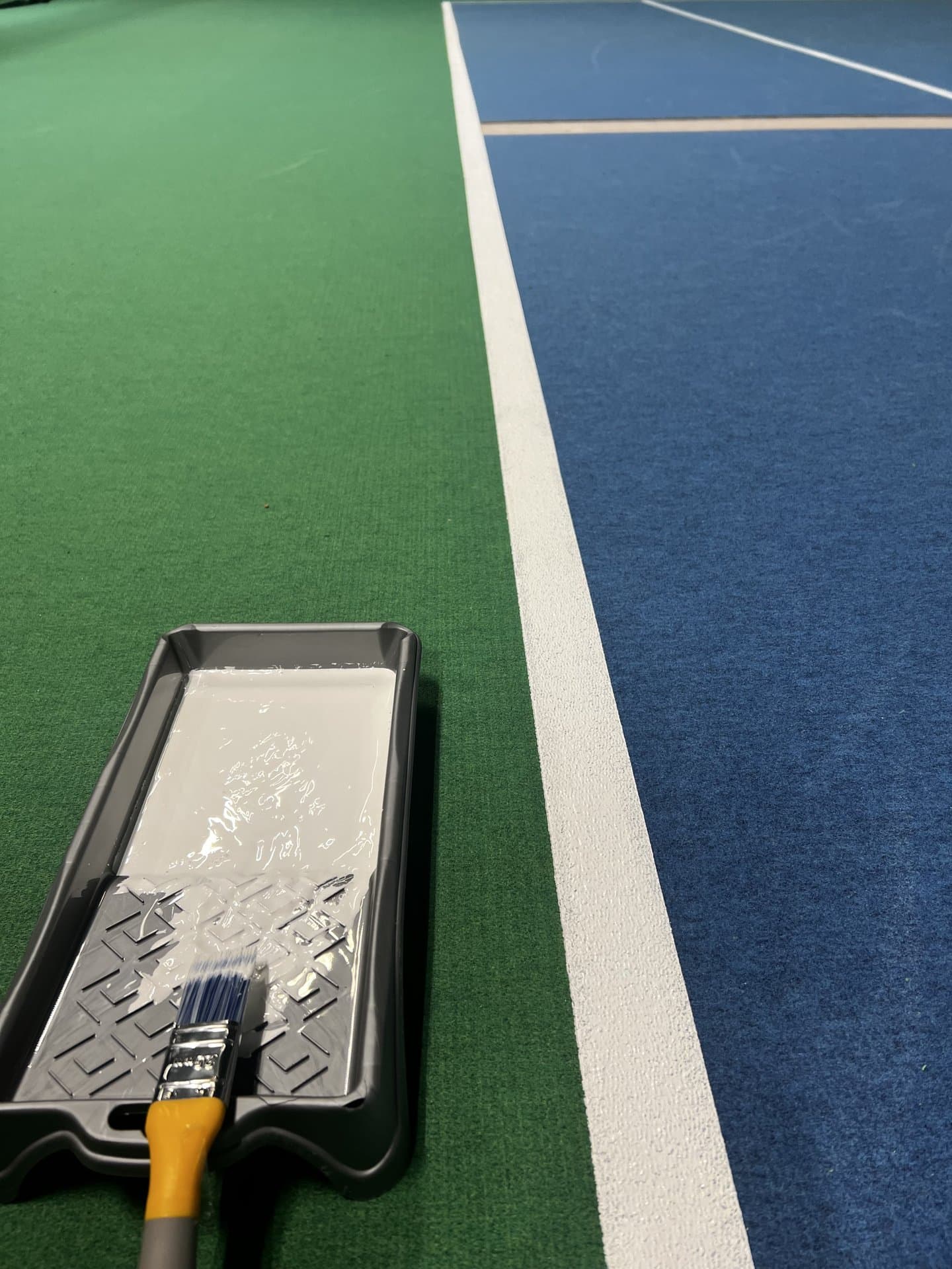 Närbild på målarbacke och pensel vid underhållsarbete på sportgolv